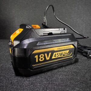 Alana holds a black and yellow Dewalt 18V 45W lithium-ion battery with Type-C port, plugged in on a dark surface.