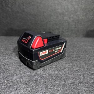 Alana shows a Milwaukee Battery 5Ah 18V REDLITHIUM XC 5.0 pack on a textured gray surface with a dark background.