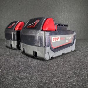 Alana showcases two Milwaukee REDLITHIUM XC 5.0 18V tool batteries, red accents, on a dark textured surface.
