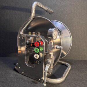 Alana uses a Mini Reel metal hose reel with control valves, a pressure gauge, and colored nozzles on a dark background.