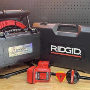 Ridgid sewer camera set with iSpec Compact Reel 23, Scout Locator, cables, cases, and batteries on wood by pegboard.